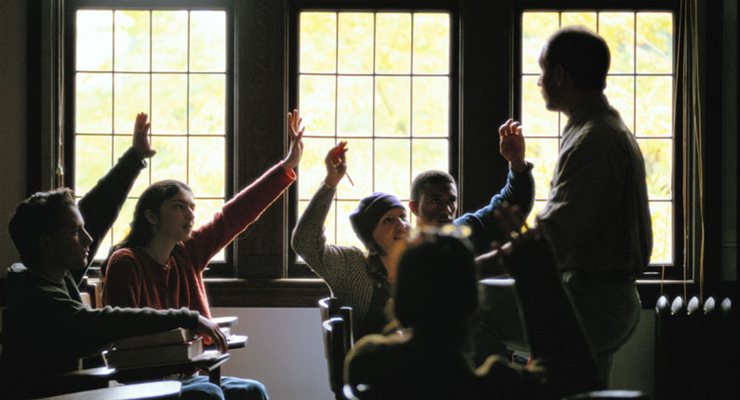 Student in classroom raising hands with teacher standing nearby
